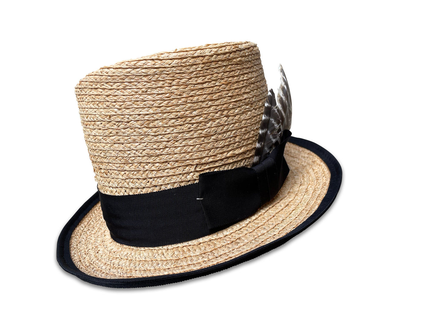 Raffia braid top hat with black ribbon trim. Left side view with bow and turkey feathers. Brim is piped with black grosgrain ribbon.