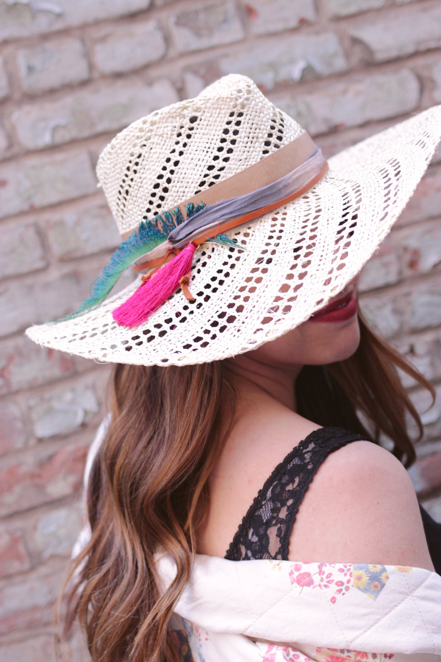 Wide brim straw hat trimmed with camel ribbon, silk sari fabric, leather cord & a hot pink tassel. Straw is woven with an open weave swirl pattern . Right side view.