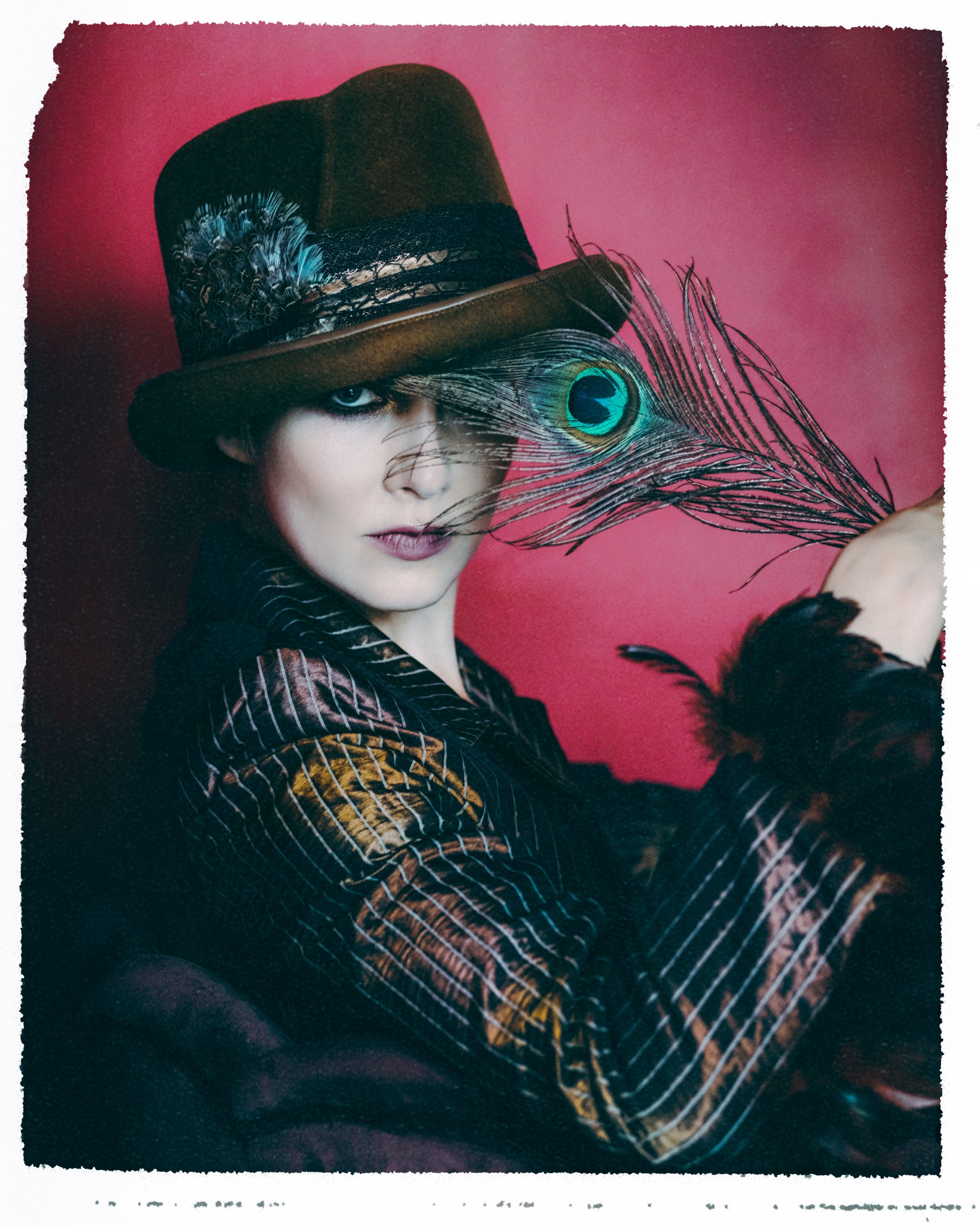 A stylized portrait of a person wearing a dark brown top hat, embellished with a black lace band, faux crocodile skin trim, and a striking pheasant feather. 
