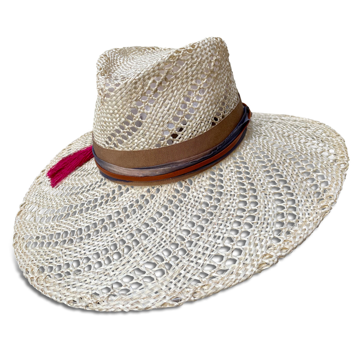 Wide brim straw hat trimmed with camel ribbon, silk sari fabric, leather cord & a hot pink tassel. Straw is woven with an open weave swirl pattern . Left side view.