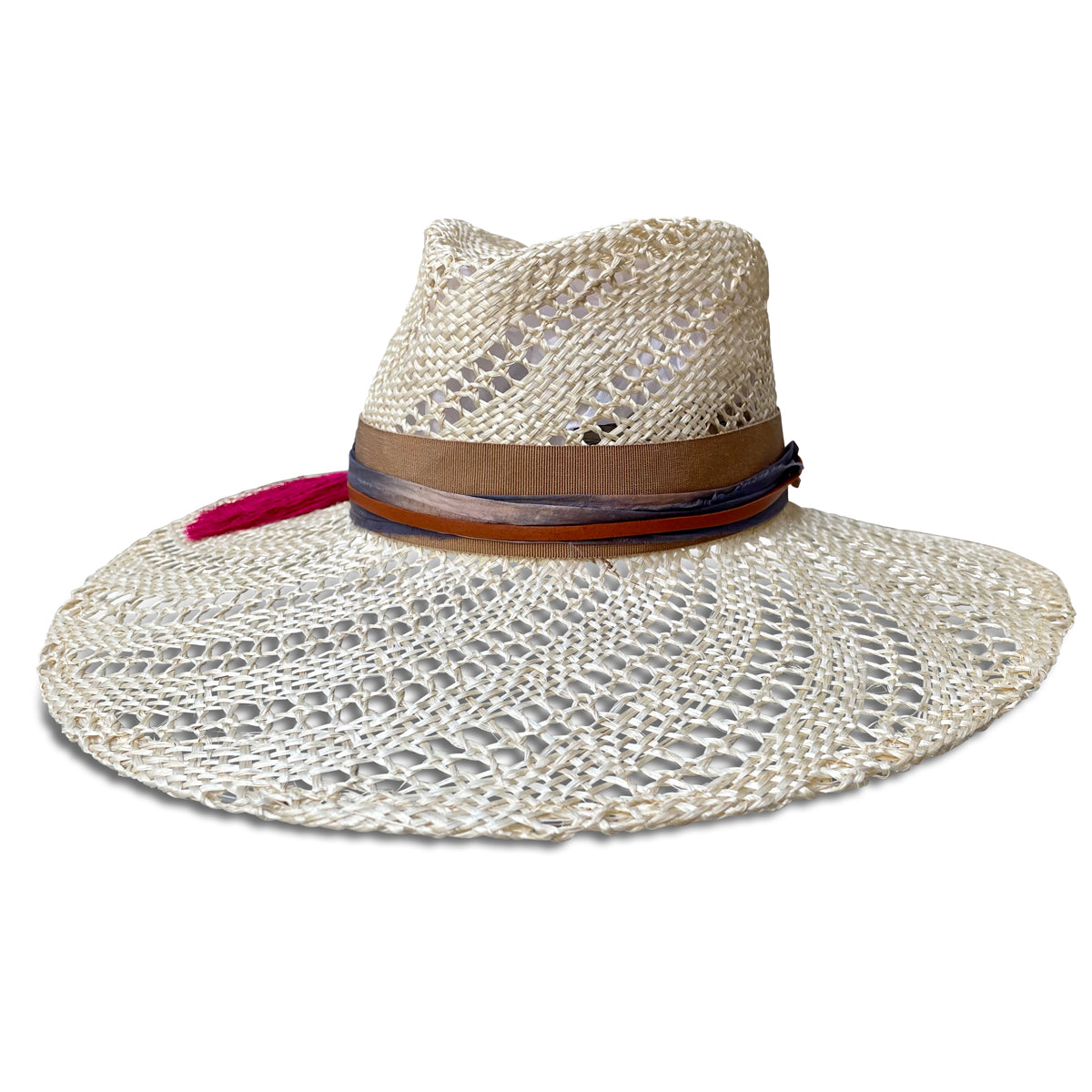 Wide brim straw hat trimmed with camel ribbon, silk sari fabric, leather cord & a hot pink tassel. Straw is woven with an open weave swirl pattern . Front view.