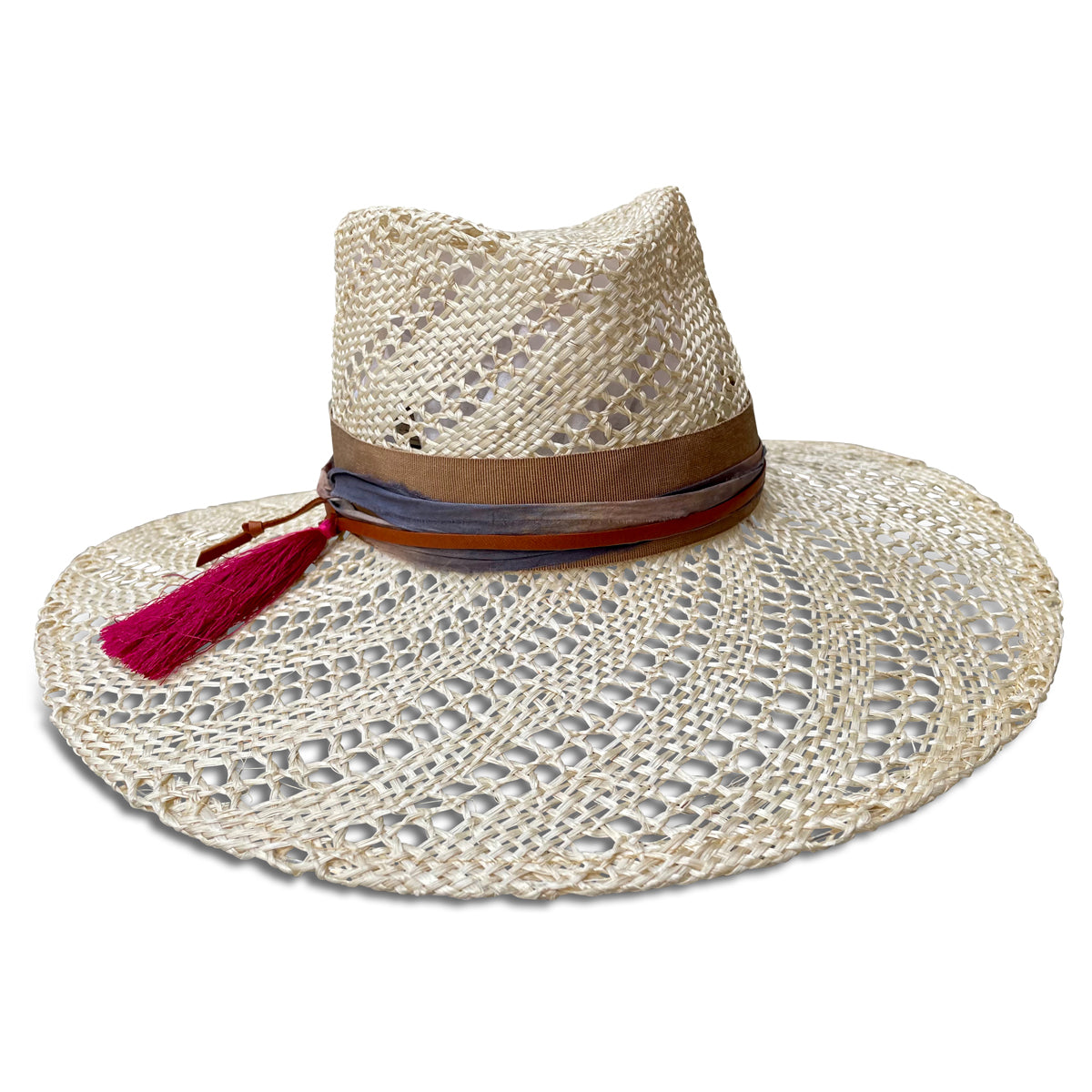 Wide brim straw hat trimmed with camel ribbon, silk sari fabric, leather cord & a hot pink tassel. Straw is woven with an open weave swirl pattern . Front view.