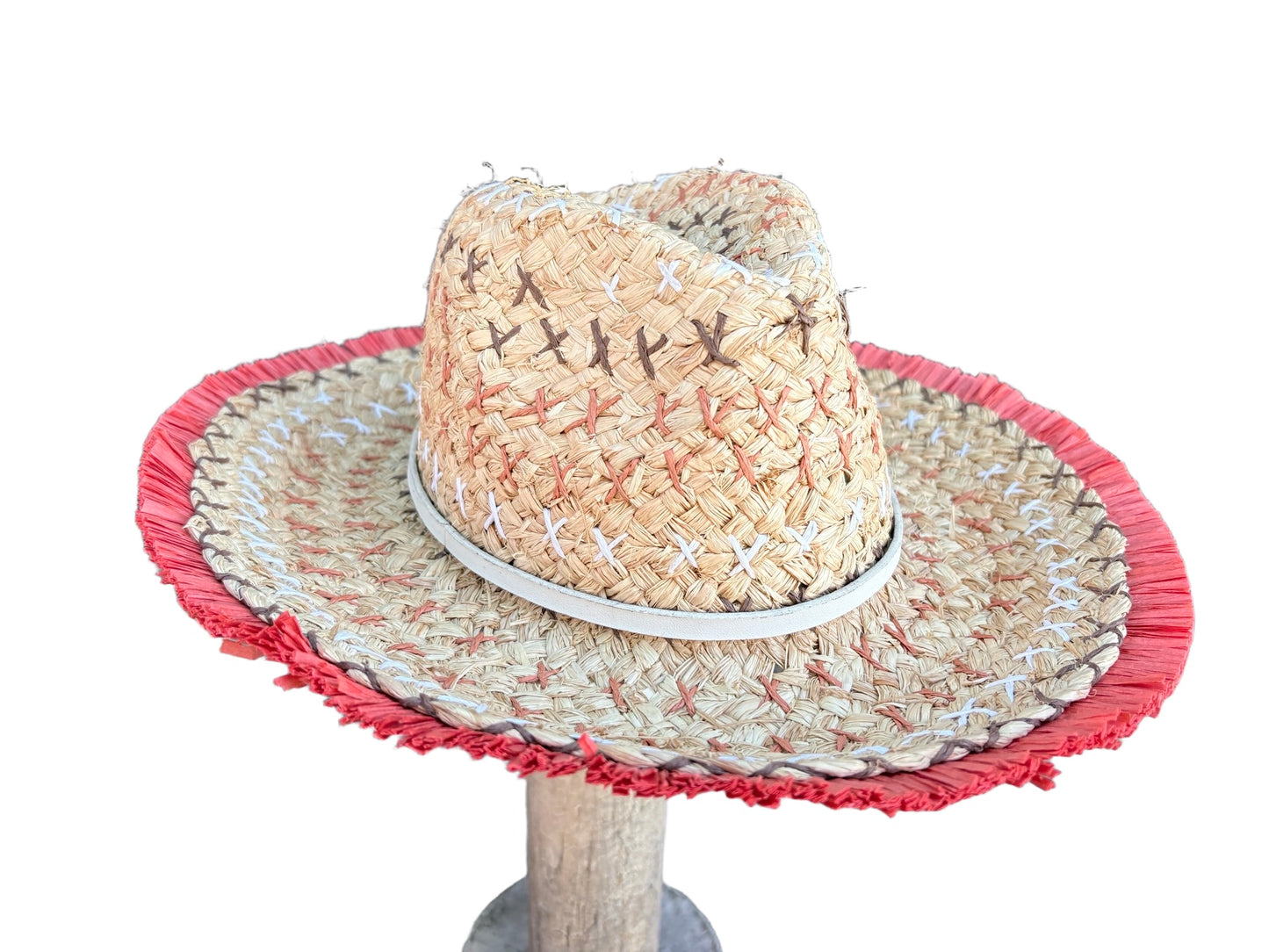 A woven straw hat with a red fringed brim and a white band, displayed on a wooden stand against a white background.