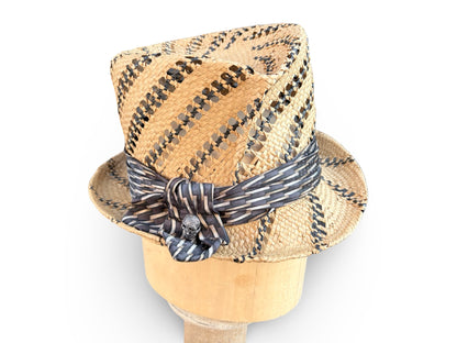 A woven straw fedora hat with black and tan diagonal stripes and a matching striped ribbon bow, displayed on a wooden mannequin head against a white background.