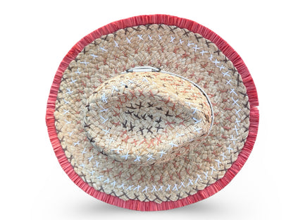 A woven straw cowboy hat viewed from directly above, featuring a natural beige straw body with white and black stitched details and a prominent red fringed border.