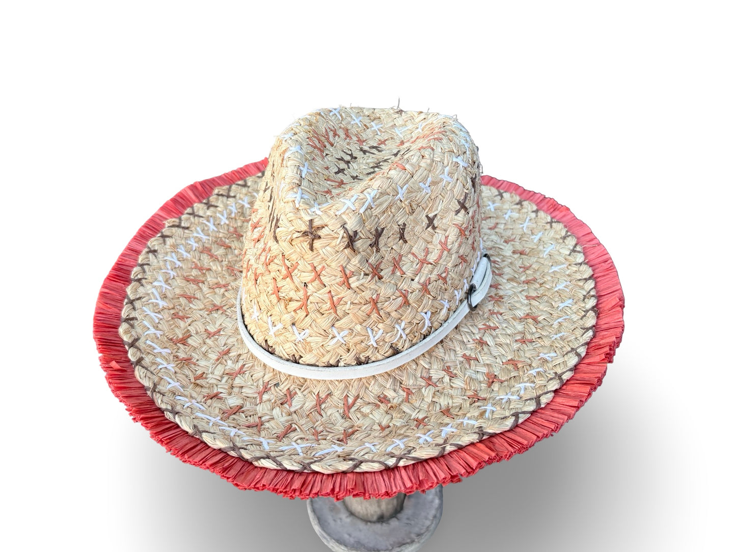 A woven straw cowboy hat with a red fringed brim and a white band, displayed on a stand against a white background.