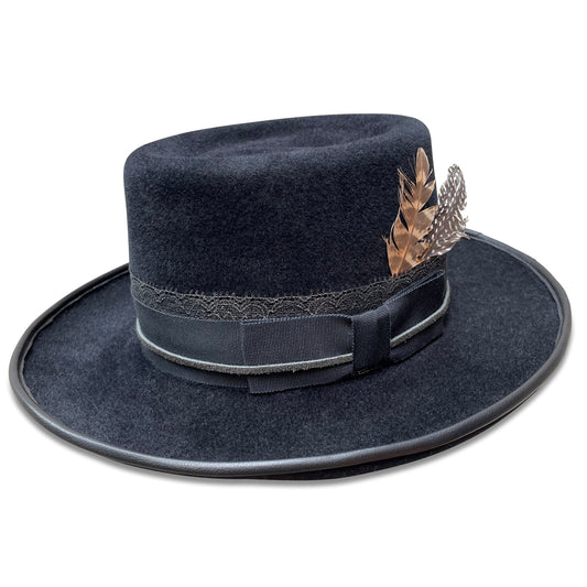 A sophisticated black felt gambler hat with a tall western-style crown and a slightly upturned brim. The hat features elegant lambskin piping, a band of metallic black lace behind black grosgrain ribbon, and is adorned with turkey and guinea hen feathers.